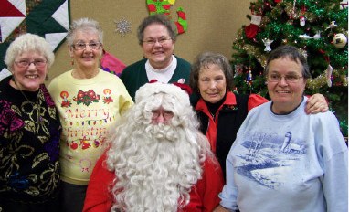 Five smiling members posing with Santa by the Christmas tree